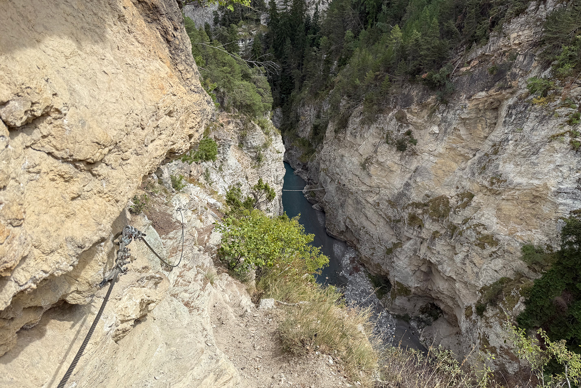 Cliffside via ferrata with a steel rope trail overlooking a steep rocky gorge and a river below.