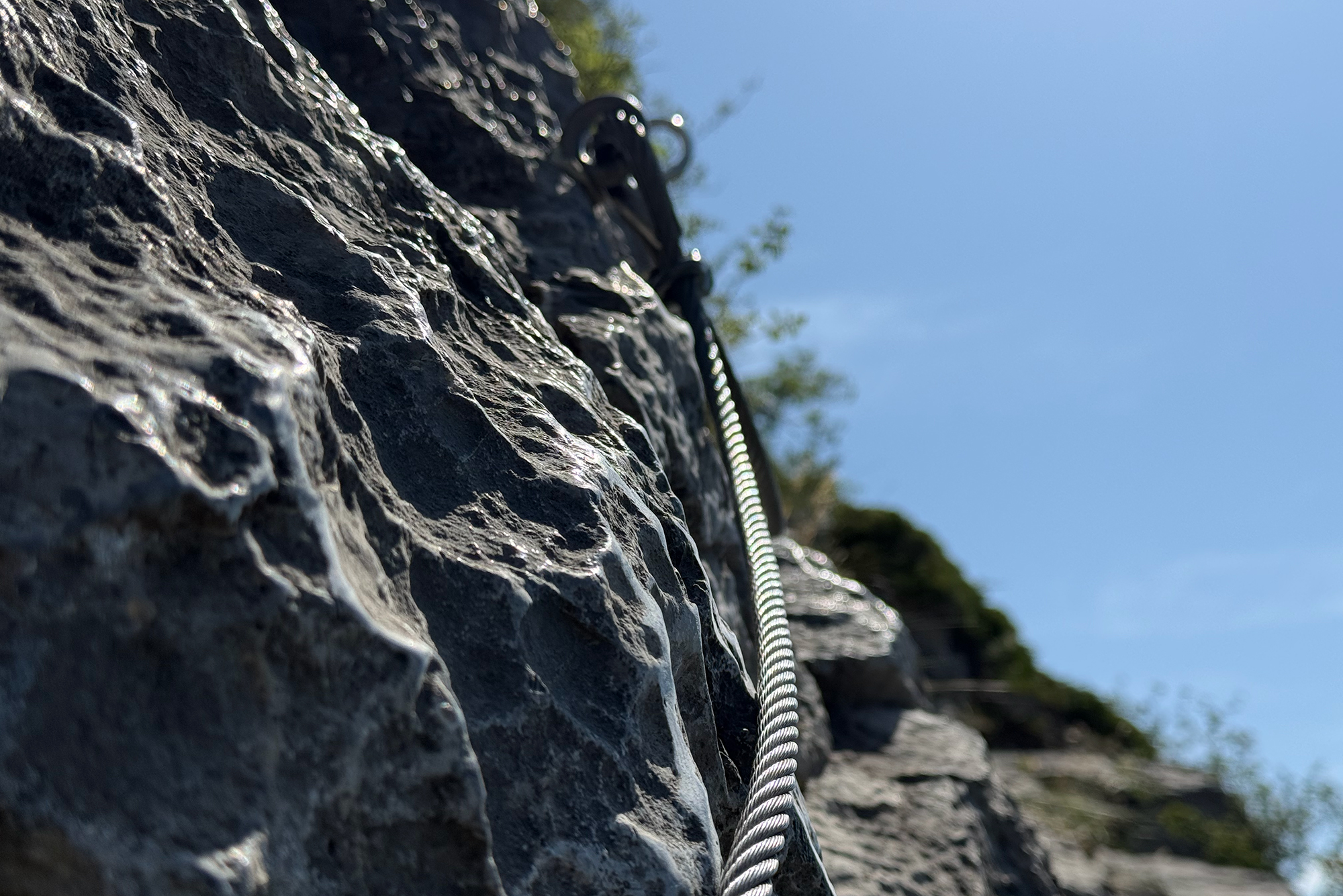 Close-up of a thick rope running along a rugged stone wall against a bright blue sky.