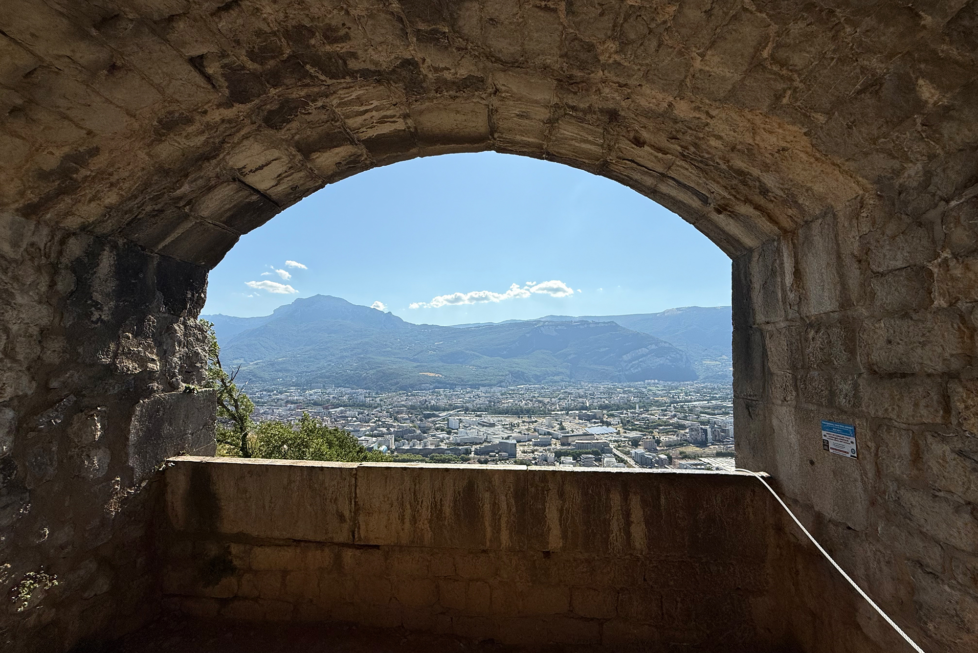 Stone archway opening to a valley city and distant mountains under a blue sky