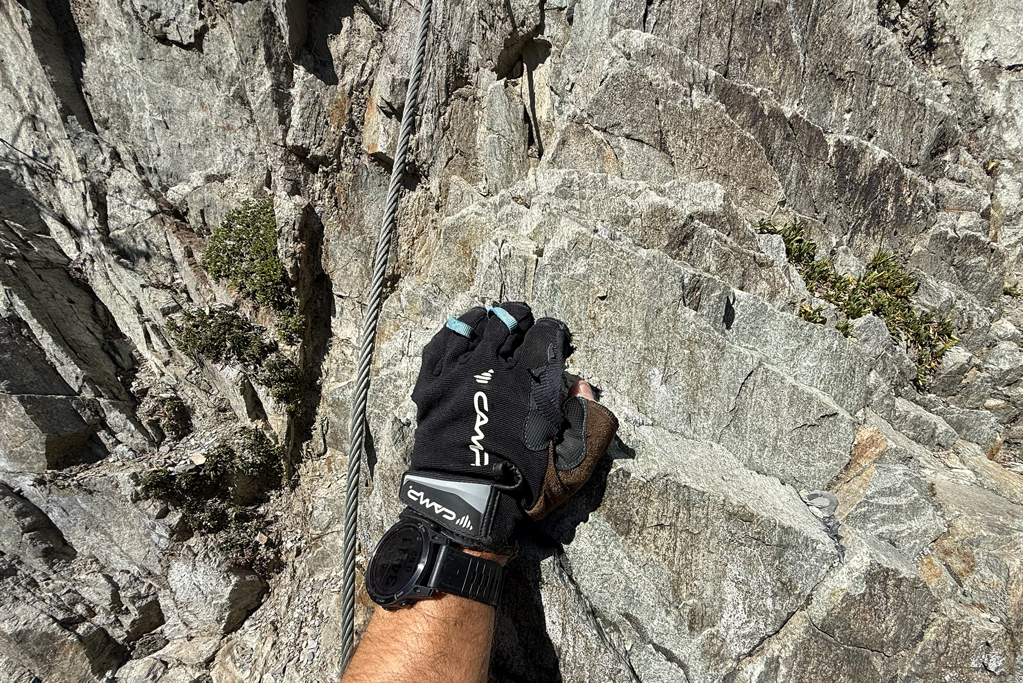 Climber's gloved hand gripping a steel rope against a gray rock cliff.