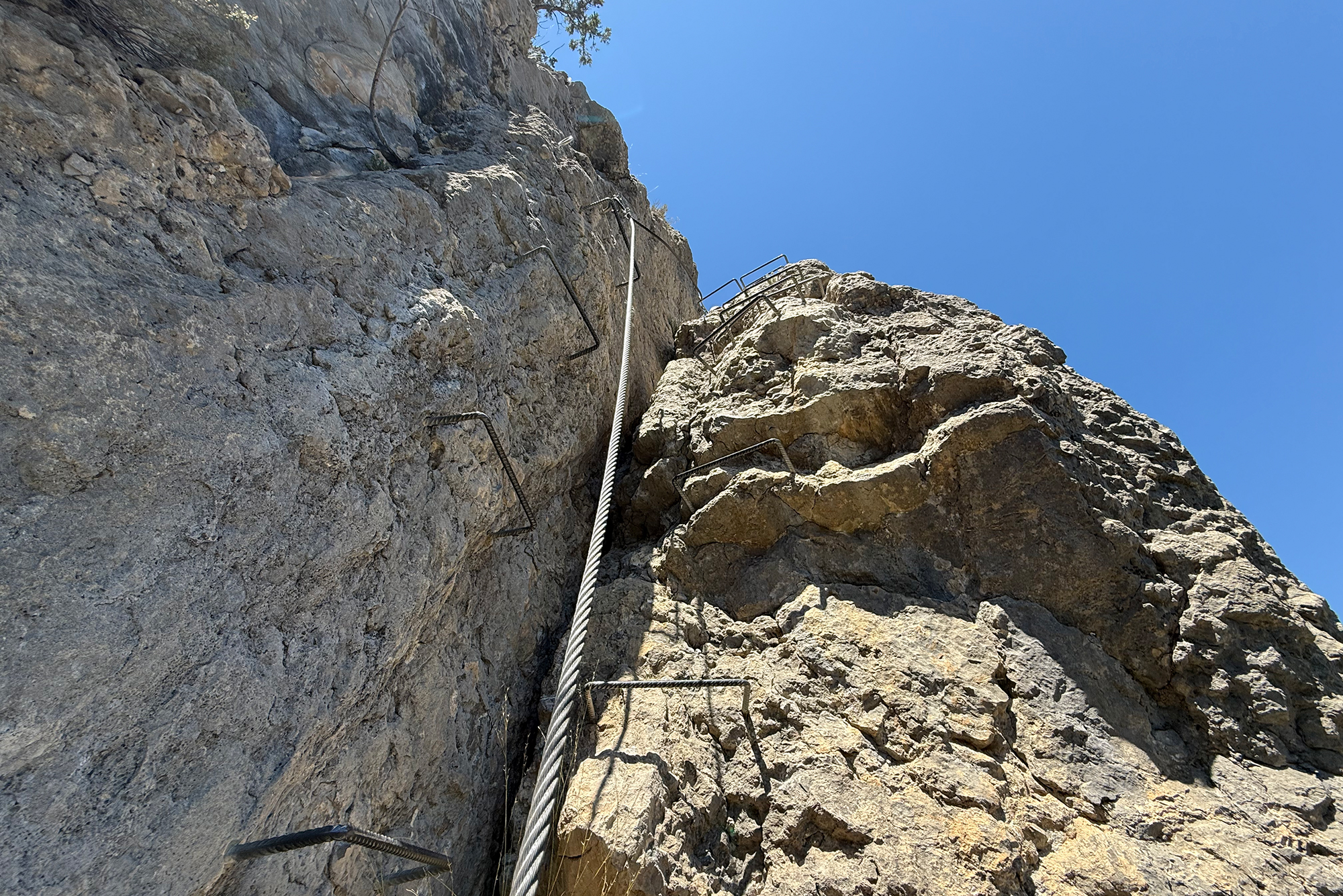 Steep rock cliff with metal cables and ladders for via ferrata climbing against a clear blue sky