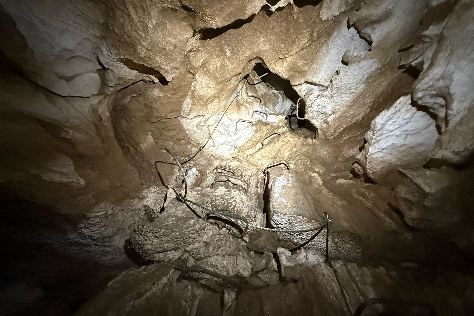 Rocky cave wall with a vertical metal ladder rungs and hanging ropes for climbing