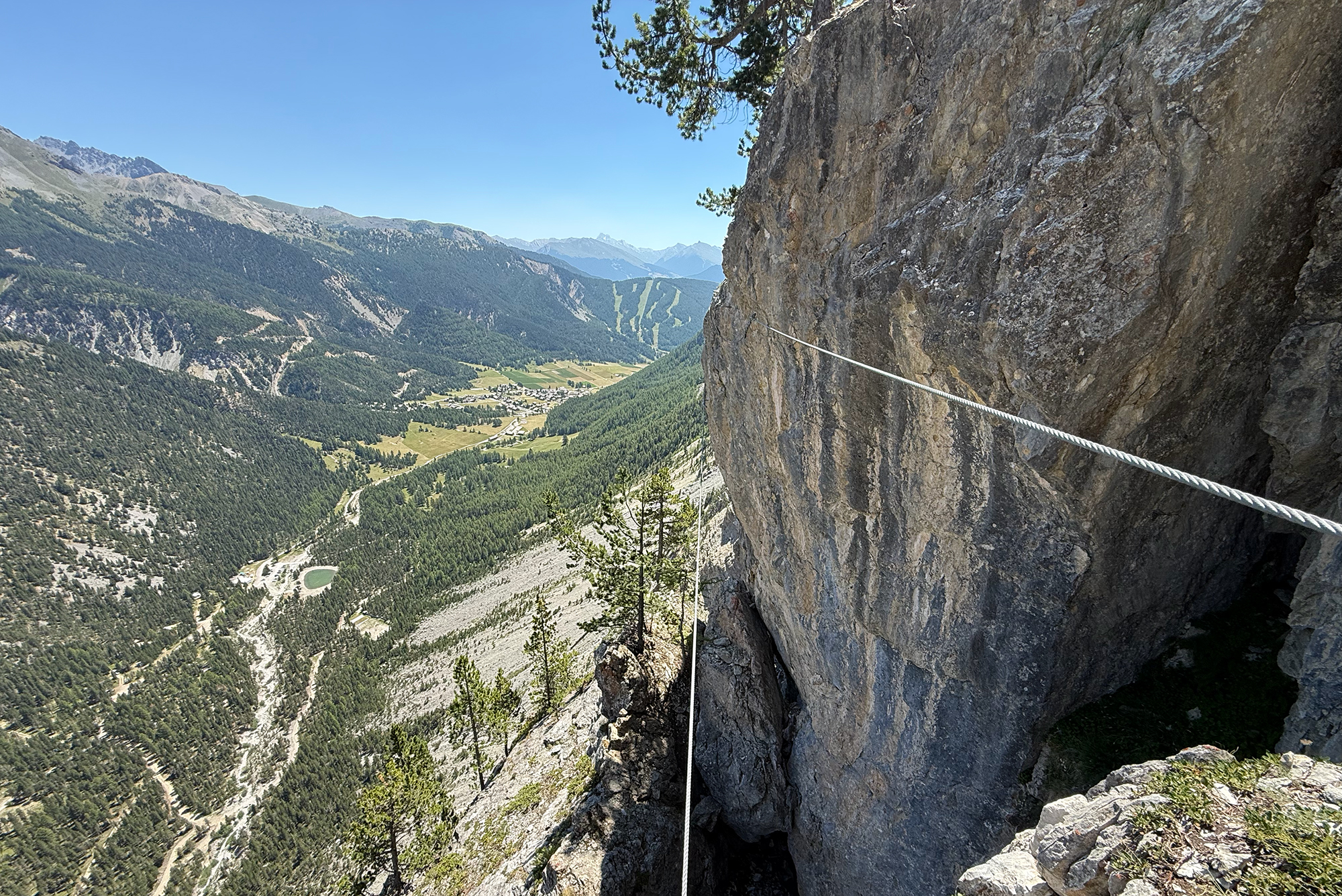 Rock cliff with safety rope dangling over a steep drop, mountain valley below