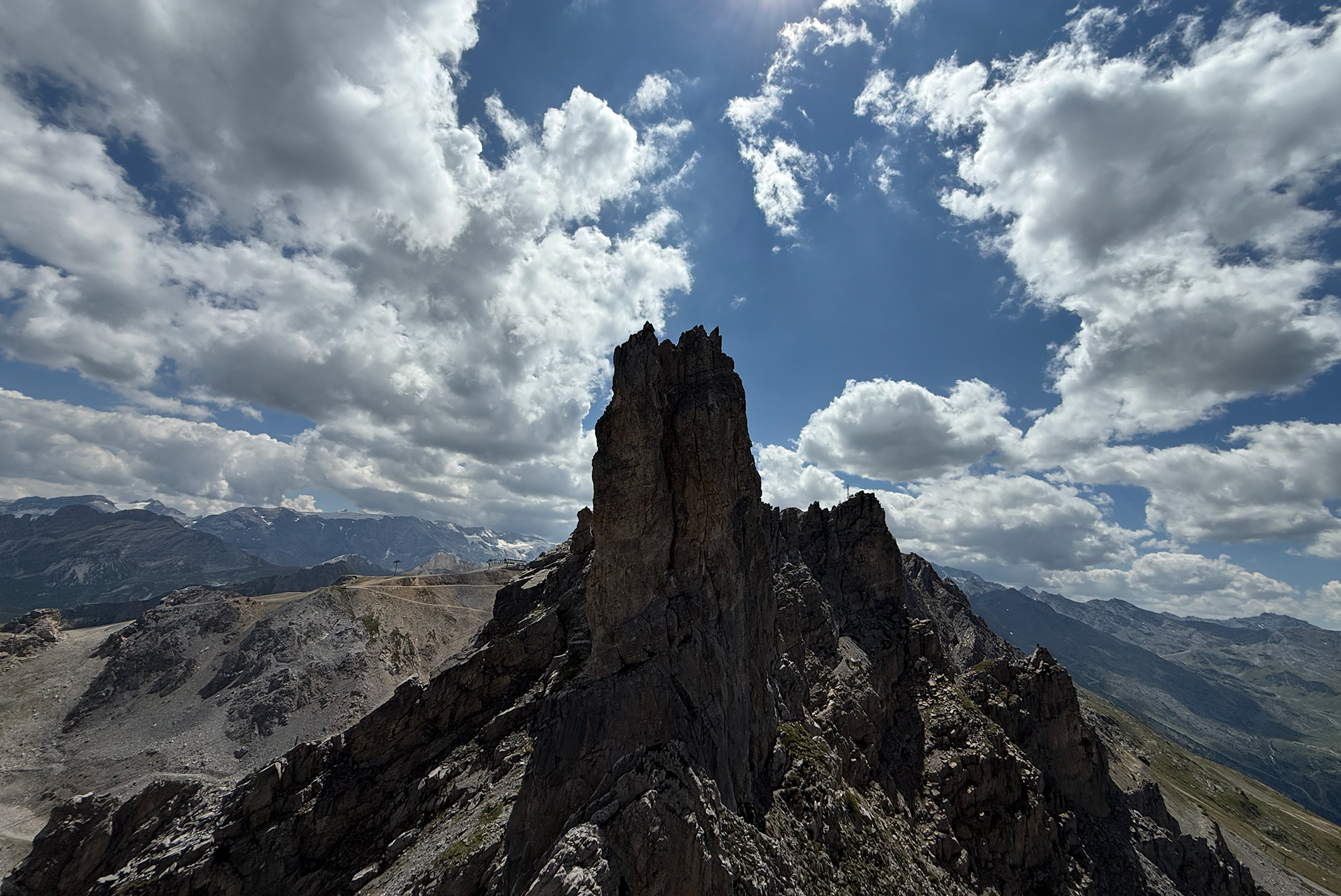 Jagged rock spire in the foreground with distant mountains and a blue, partly cloudy sky