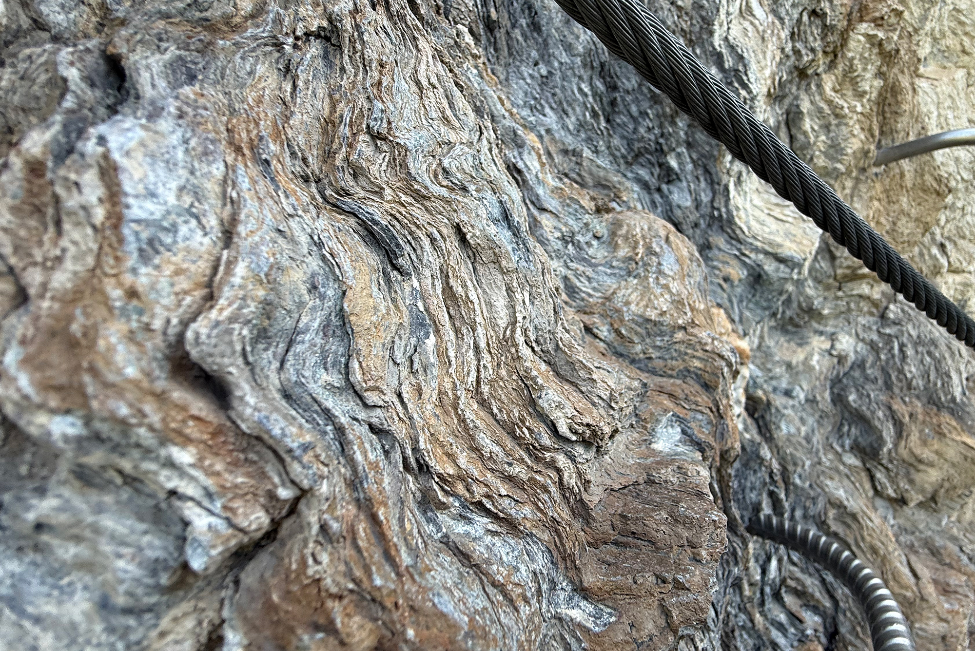 Close-up of a rugged rock surface with a braided steel cable crossing diagonally across the frame.