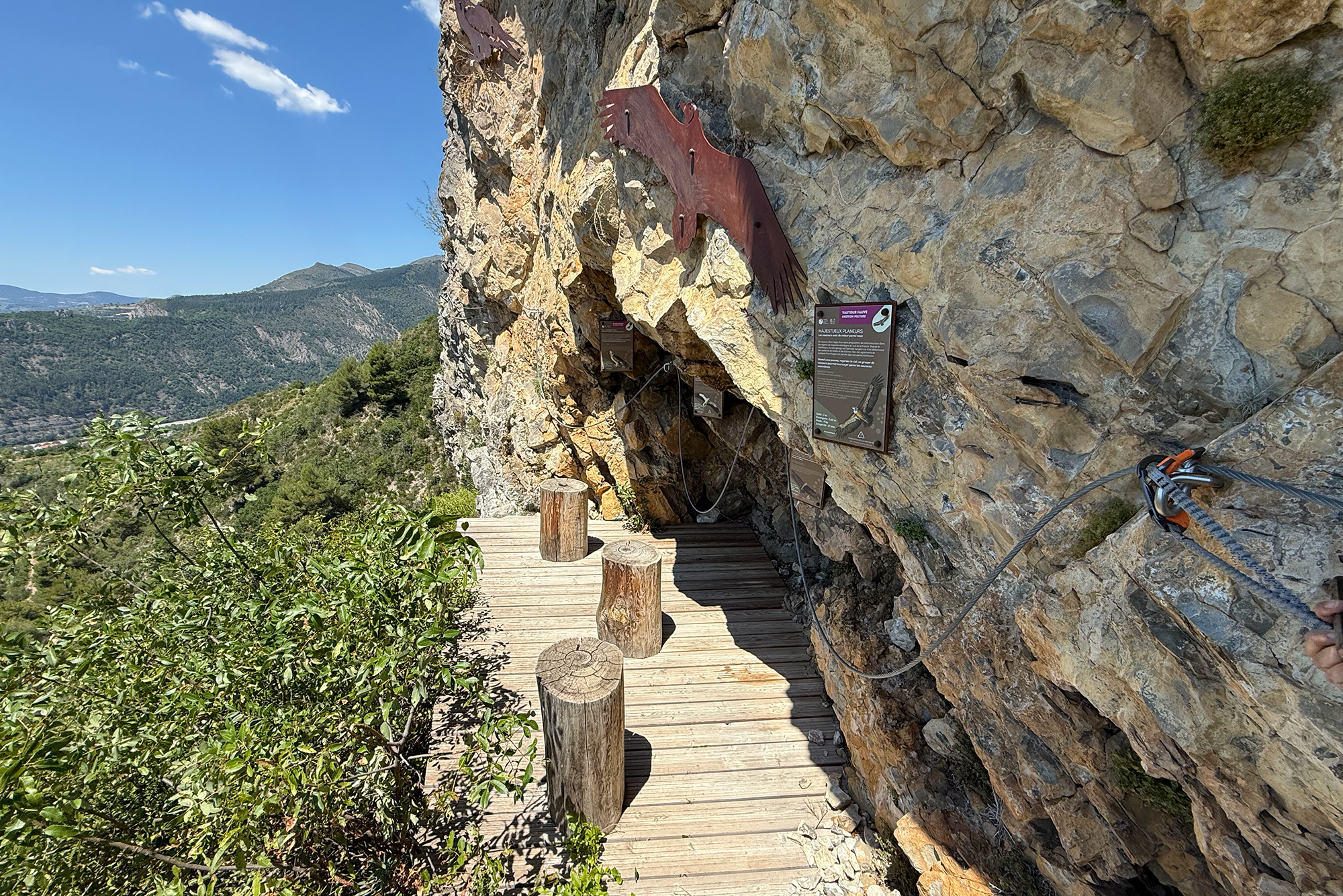 Rusty metal silhouette of a flying bird mounted on a rocky cliff next to a wooden boardwalk and informational signs.