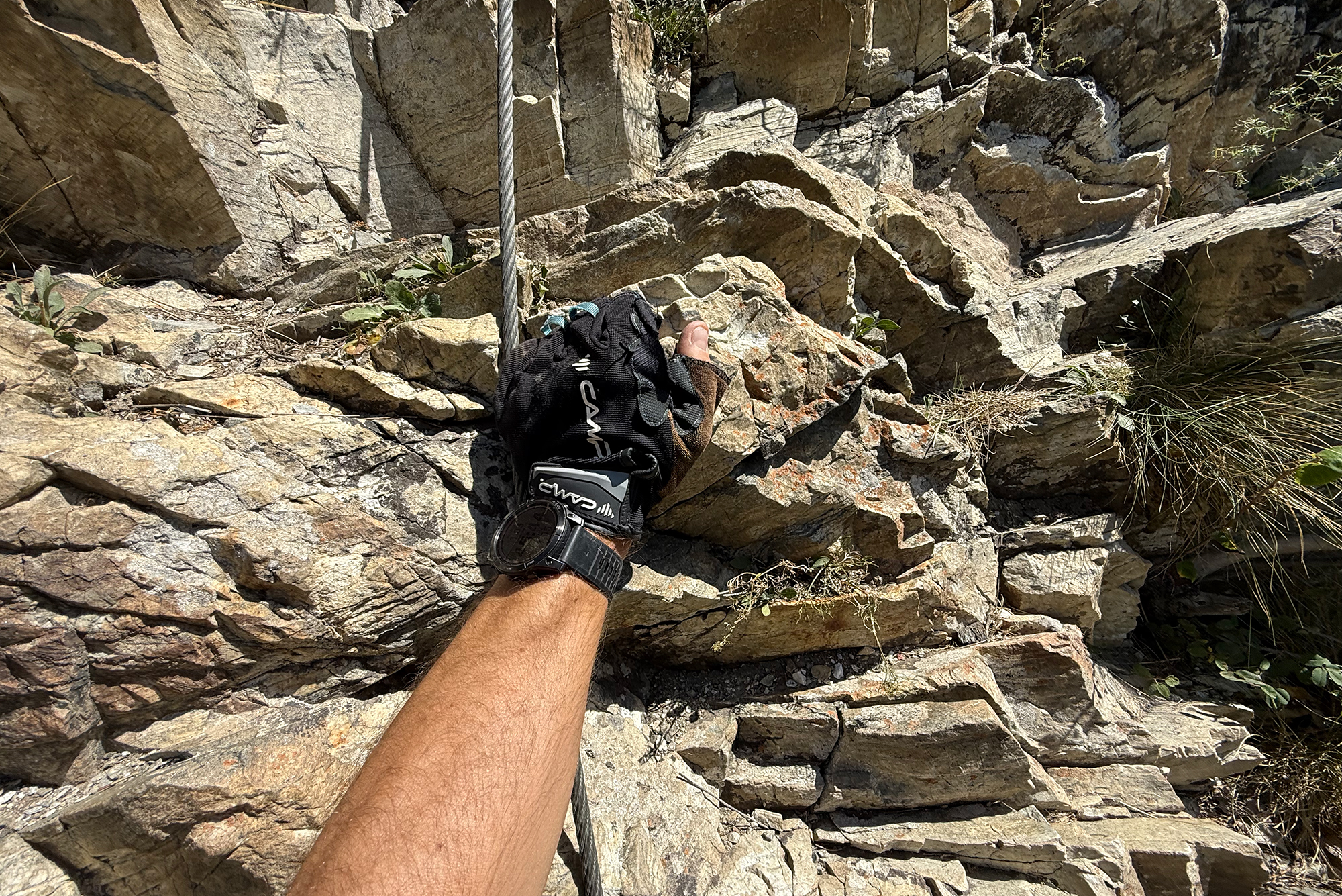 Climber's gloved hand gripping a rope against a rough rock wall.