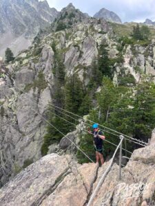Climber wearing a blue helmet crosses a rocky mountain via ferrata with steel cables and railing.
