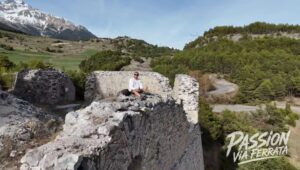 Person sitting on a stone ruin overlooking a valley with snow-capped mountains in the distance.